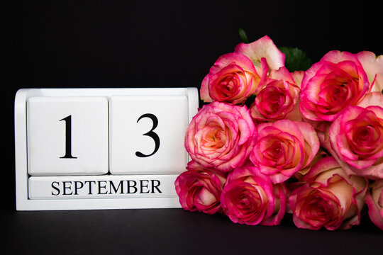 September 13 wooden calendar, white on a black background, pink roses lie nearby.Postcard with copy space. The concept of a holiday, congratulation, invitation, party, announcement, vacation,promotion