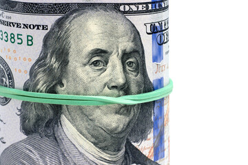 Rolled hundred dollar bills are tied with a green banker's rubber band. Portrait of Franklin...