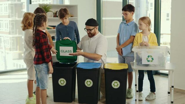 Garbage sorting class, a young teacher tells and explains to children how and where to sort garbage, shows inscriptions to make it easier to sort and shows finger up to the childrens
