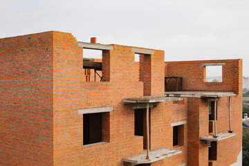 Construction of an apartment building with red bricks against a white sky. Unfinished brick house. High-rise red brick building. 