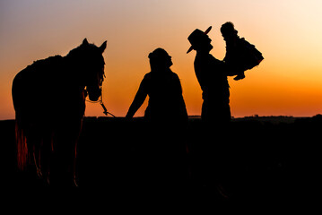 silhouette of farm family, woman holding horse and gaucho father holding daughter