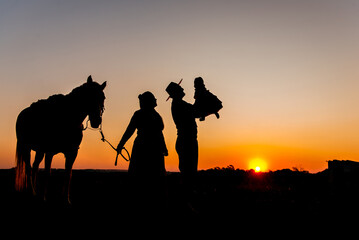 Silhouette of horse and gaucho family at sunset in the countryside.