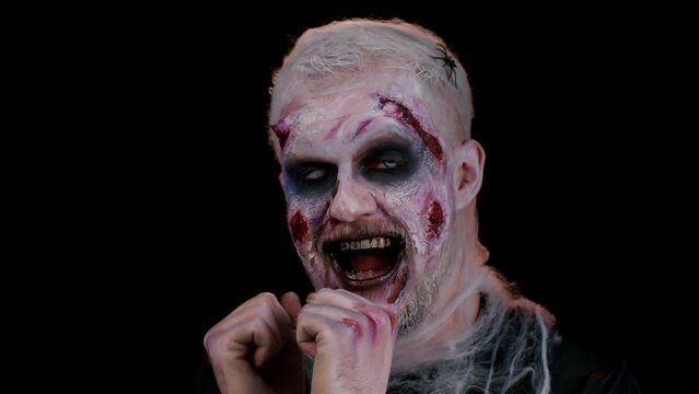 Portrait of sinister man in carnival costume of Halloween crazy zombie listening music, smiling dancing to disco music rhythmically moving her hands, having fun. Horror theme of cosplay undead monster