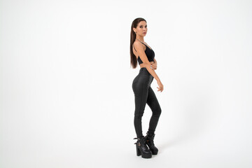 a brunette girl with long hair in black leather pants and boots poses on a white background.youth...