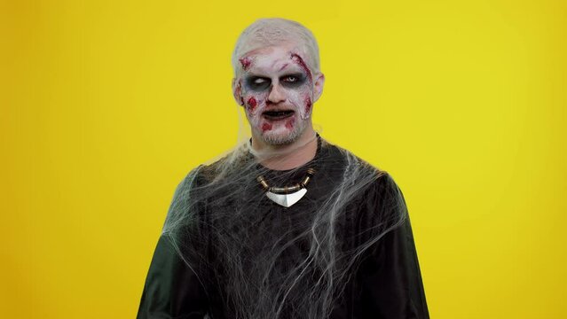Scary wounded undead guy rising head, looks at camera and smiles terribly with dirty teeth. Cheerful happy creepy man with bloody scars face, Halloween stylish zombie make-up. Sinister beast, monster