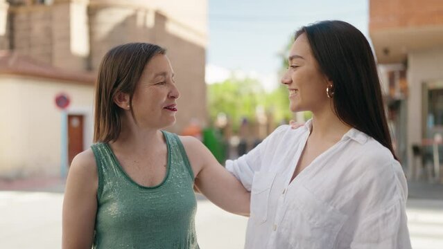 Two women mother and daughter smiling confident speaking at street