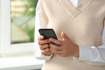 Woman using smartphone near window indoors, closeup