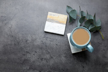 Mug of coffee, stylish cup coasters and eucalyptus branch on grey table, flat lay. Space for text