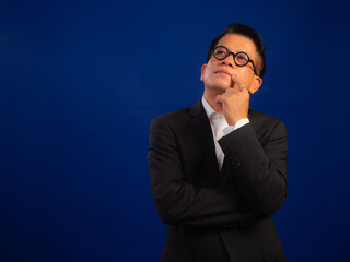 Portrait of smart middle-aged asian confident successful businessman wearing suit thinking about something with copyspace on blue background, looking attractive and positive professional leadership