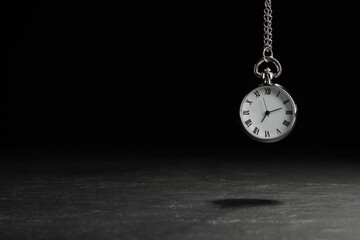 Beautiful vintage pocket watch with silver chain on black background above dark table, space for text. Hypnosis session - obrazy, fototapety, plakaty