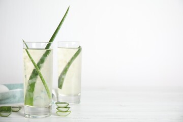 Fresh aloe drink with leaves in glasses on white wooden table. Space for text