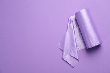 Roll of color garbage bags on violet background, top view. Space for text