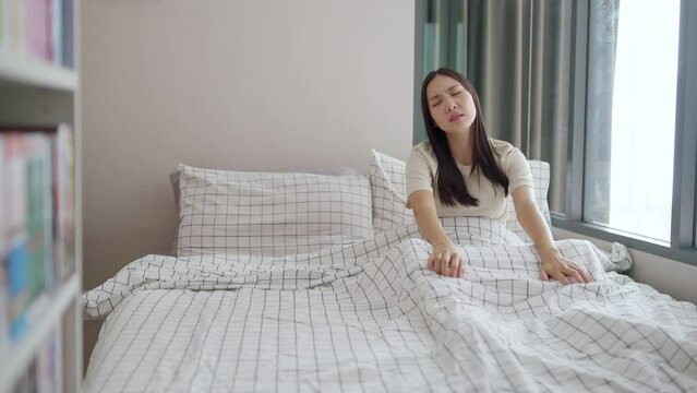 4K Sleepy young Asian woman in pajama wake up in the morning with unhappy. Attractive girl feeling sick and sleepless while waking up on the bed in the morning. Mental health care and insomnia concept