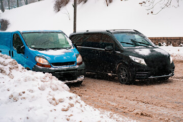 Two minivans move through a covered city of snow with a huge heap of snow near the road. Unclean. Snow. City. Winter. Street. Outdoor. Transportation. Blizzard. Heap. Climate. Weather. White. Problem