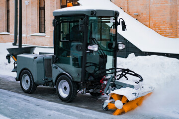 City service cleaning snow, a small tractor with a rotating brush clears a road in the city park...