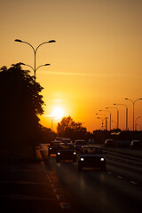 Silhouettes of vehicles moving in city traffic against the setting sun.