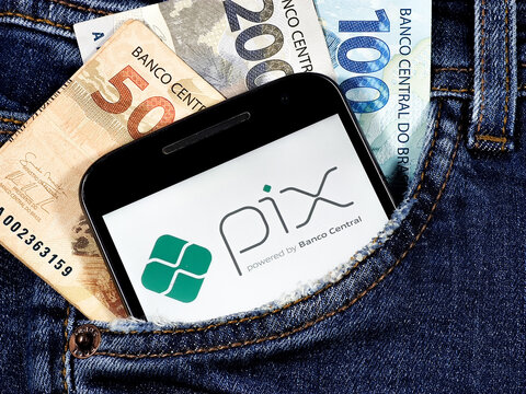 Smartphone with Pix logo on the screen in jeans pocket with notes of 100 reais 200 reais and 50 reais. Pix is ​​the Brazilian instant payment