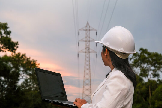 Asian female electrical engineer working on laptop near high voltage pole, inspecting power grid. Wind Turbine Engineer for Electric Power Generation. renewable energy concept