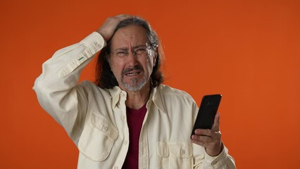 Man with mobile cell phone smartphone typing browsing, loses becoming surprised sudden lottery results, bad fortune, loss, man on orange background. People sincere emotion