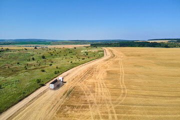 Fototapeta na wymiar Aerial view of lorry cargo truck driving on dirt road between agricultural wheat fields. Transportation of grain after being harvested by combine harvester during harvesting season