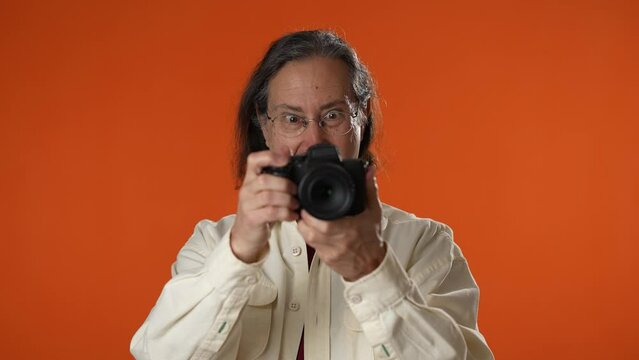 Smiling happy man taking photos video with a camera isolated on a solid orange background.