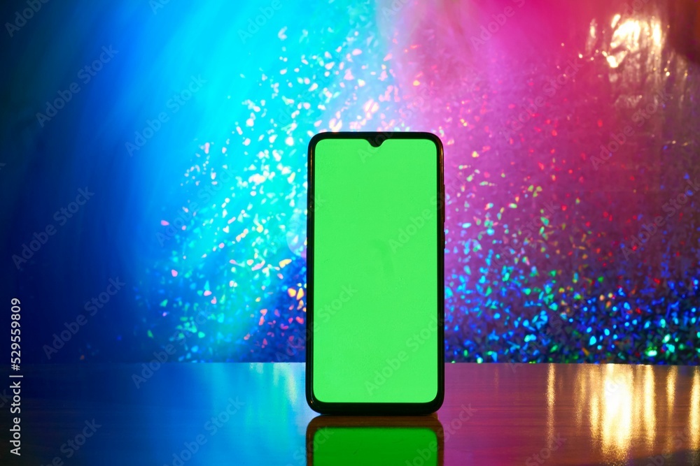 Poster cellular phone with a green screen on a wooden table isolated from a colorful background