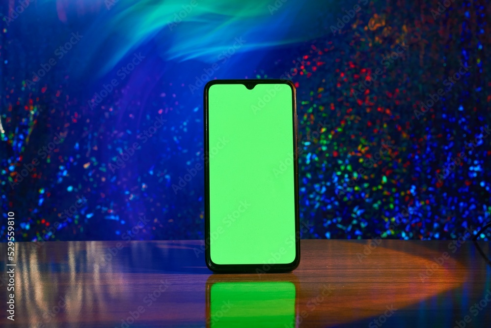 Poster cellular phone with a green screen on a wooden table isolated from a colorful background
