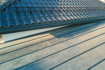 Closeup snow guard for safety in winter on house roof top covered with ceramic shingles. Tiled covering of building