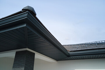 House corner with brown metal planks siding and roof with steel gutter rain system. Roofing,...