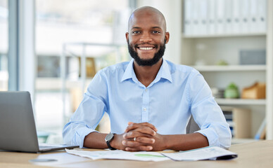 Obraz premium Portrait of a happy African businessman sitting at his desk in his modern corporate office. Professional black manager working or planning a company project with a laptop and paperwork at a table.
