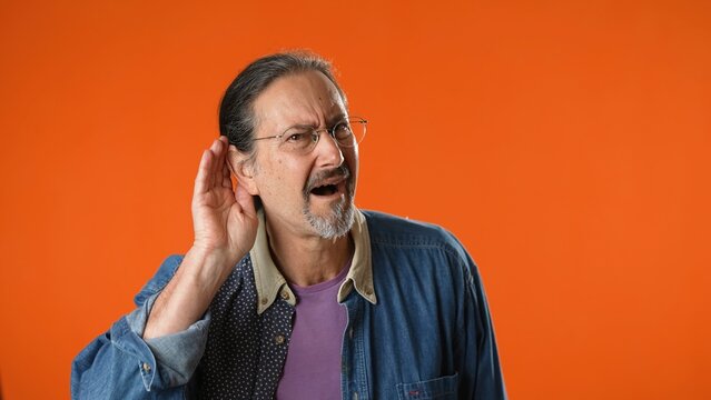 Man Struggles To Hear, Having Difficulty Hearing, Isolated On Solid Orange Background Studio Portrait.