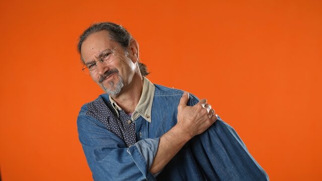 Sick Ill Sad Tired Portrait Of Man Put Rub Arm Muscles Having Pain Suffering From Soreness Isolated On Solid Orange Background Studio Portrait