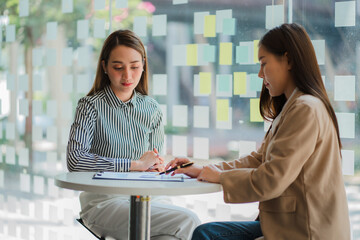 Two Asian business women talk, discuss strategies at office marketing workshop concept.