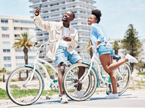 Selfie, bike and date with a couple cycling on a promenade during summer with love, romance and affection. Bicycle, photograph and fun with a black woman and man outside and a city in the background