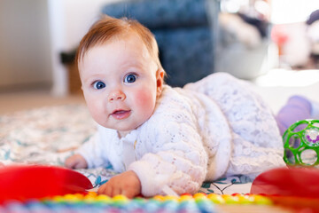 Happy baby girl with bright blue eyes playing with colourful abacus beads
