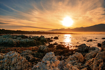 Dramatic orange  cloudscape  sunset at  dusk over the rocks and bay at Kaikoura harbour