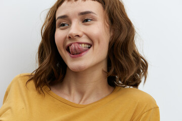 horizontal close-up portrait of a beautiful, playful, tanned woman in a yellow T-shirt on a light background amusingly showing her tongue to the camera smiling broadly