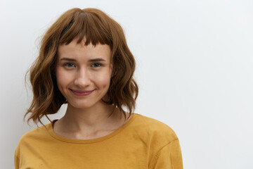 a beautiful, sweet, relaxed woman stands on a light background in a yellow T-shirt and looks at the camera with a pleasant smile. Horizontal photo with empty space