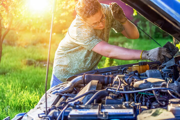 A guy repairs a motor of car at sunset in a country area