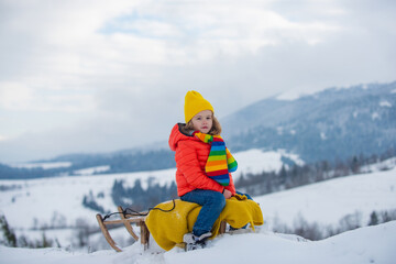 Active winter outdoors games for kids. Happy Christmas vacation concept. Boy enjoying winter, playing with sleigh ride in the winter forest.