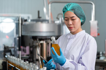 Manufacturer checking product bottles fruit juice on the conveyor belt in the beverage factory. Woman worker checks product bottles in beverage factory. Inspection quality control
