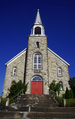 Facade and steeple of an old stone Roman Catholic church in a village in western Quebec