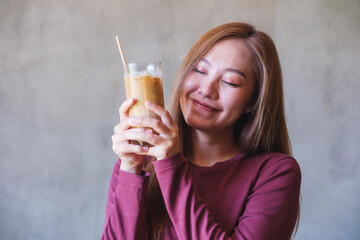 Portrait image of a young woman with closed eyes holding and drinking iced coffee