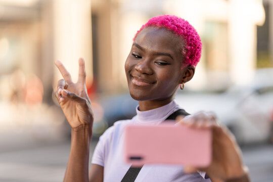 Smiling african woman taking selfie while gesturing victory outdoors