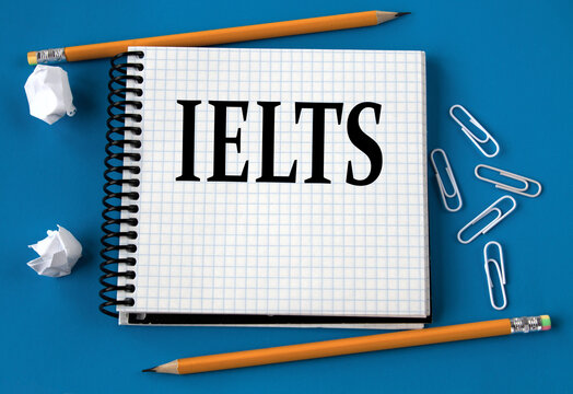 IELTS - word in a white notebook on a blue background with pencils, paper clips