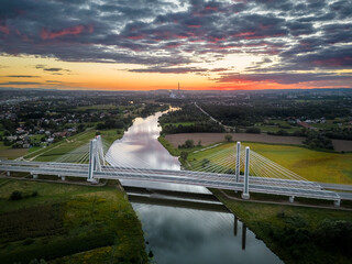 Oświetlony most nad rzeką w czasie zachodu słońca - obrazy, fototapety, plakaty