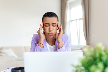 Exhausted businesswoman having a headache in home office. African American creative woman working at office desk feeling tired. Stressed business woman feeling eye pain while overworking