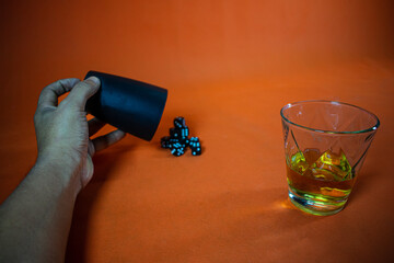 Human Hand throws dice from a glass, on the table a glass full of whiskey on an orange background