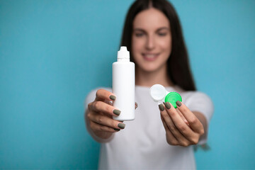 Young woman with contact lenses and bottle of solution on color background