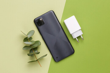 Eco gadgets. Smartphone with a charging adapter and a sprig of eucamlyptus on a green background....